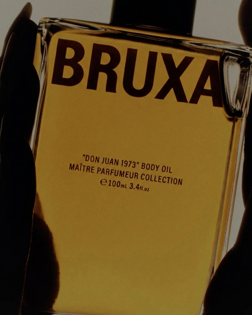 Bruxa body oil bottle held by a hand with a dark background