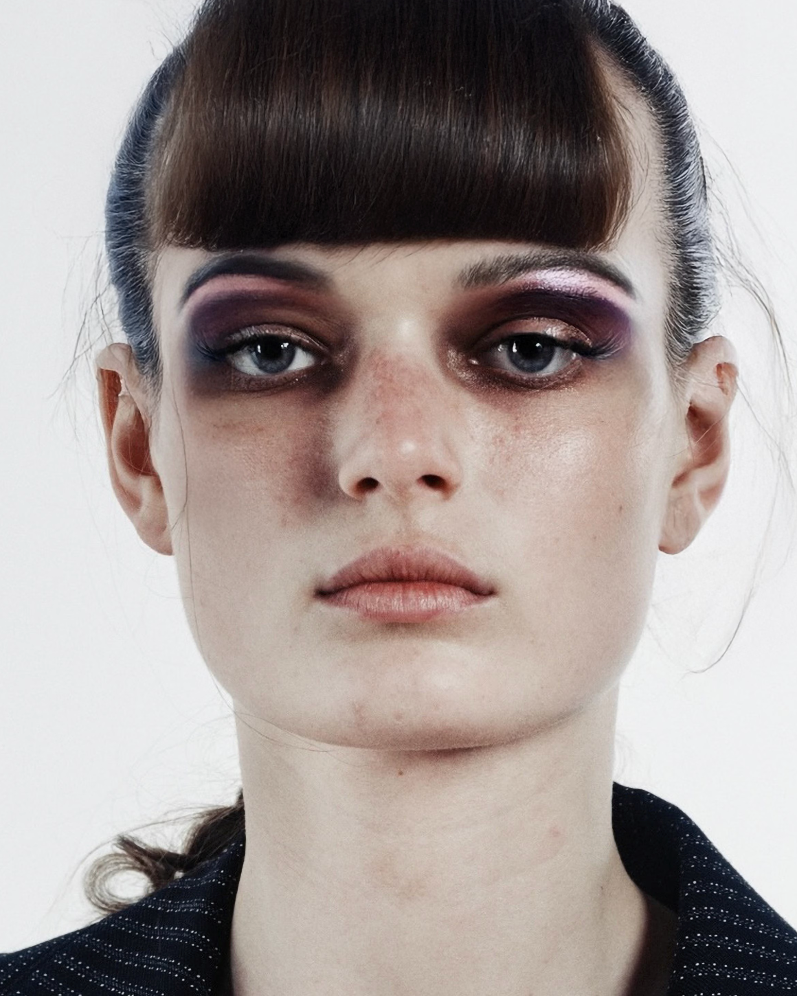 Close-up of a person with dark hair and purple eye makeup on a white background