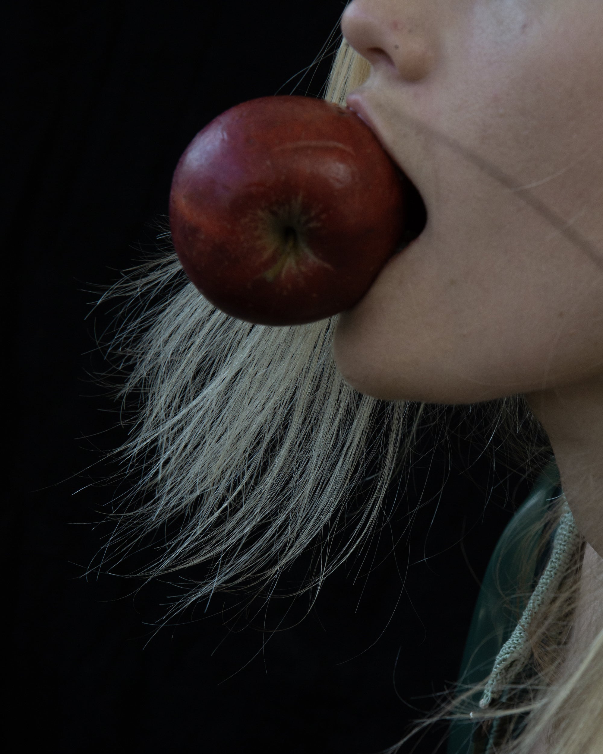 Close-up of a person holding a red apple near their mouth against a dark background