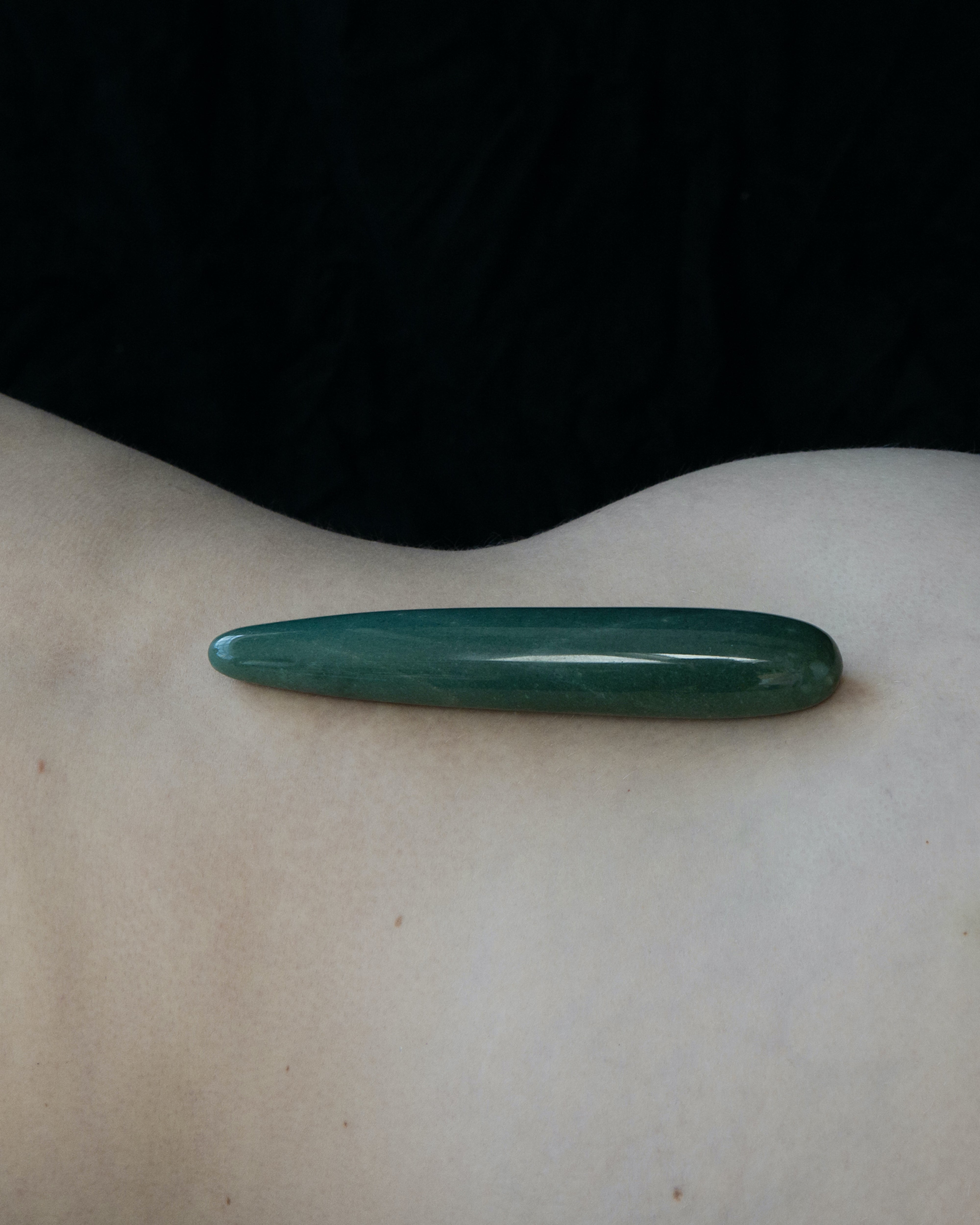 Green stone tool on a person's back against a black background