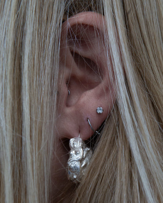 Close-up of an ear with multiple silver earrings against a blurred background