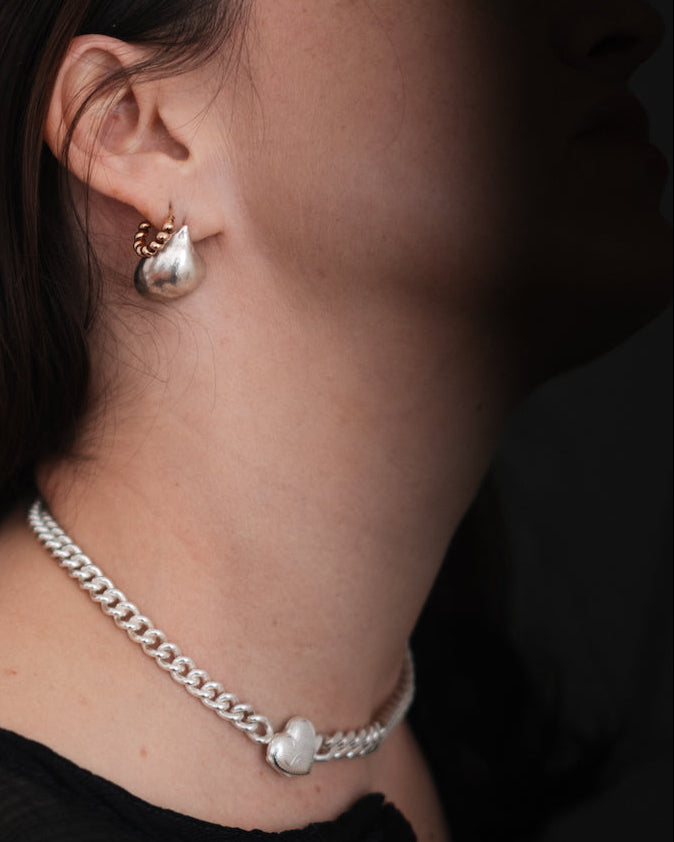 Close-up of a person wearing a silver chain necklace and gold cat-shaped earrings.