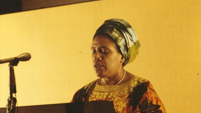Woman speaking at a podium with a microphone against a yellow background