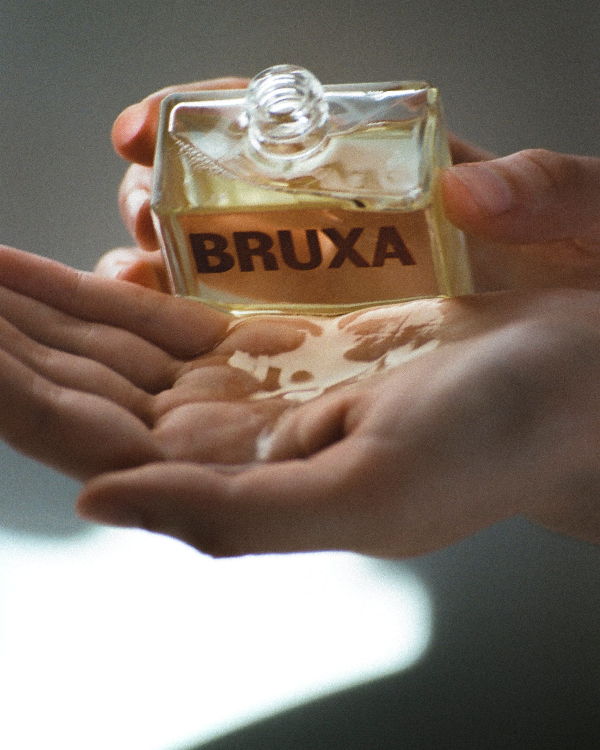 Hand holding a bottle of BRUXA perfume with a blurred background
