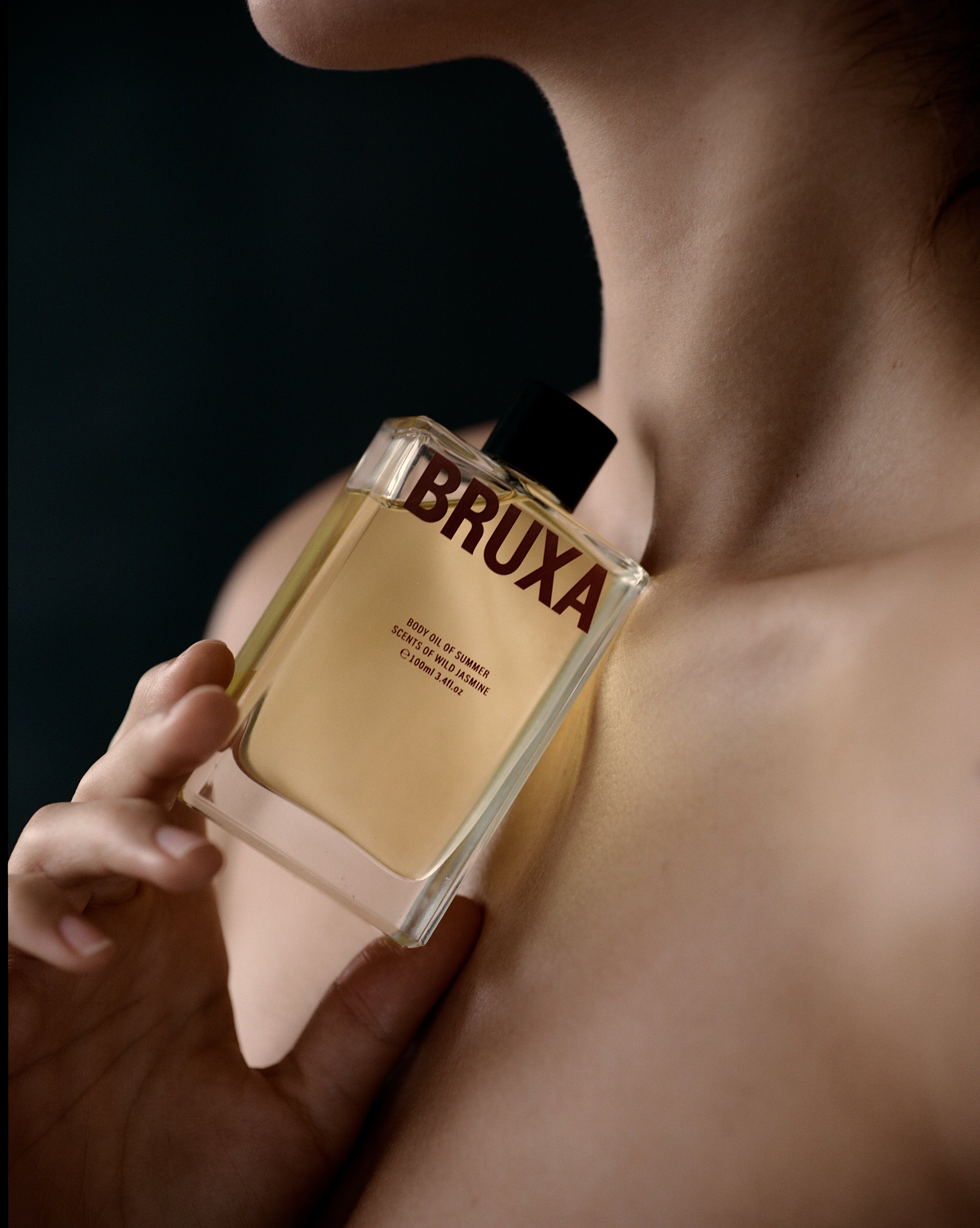 Person holding a 'BRUXA' perfume bottle against a dark background