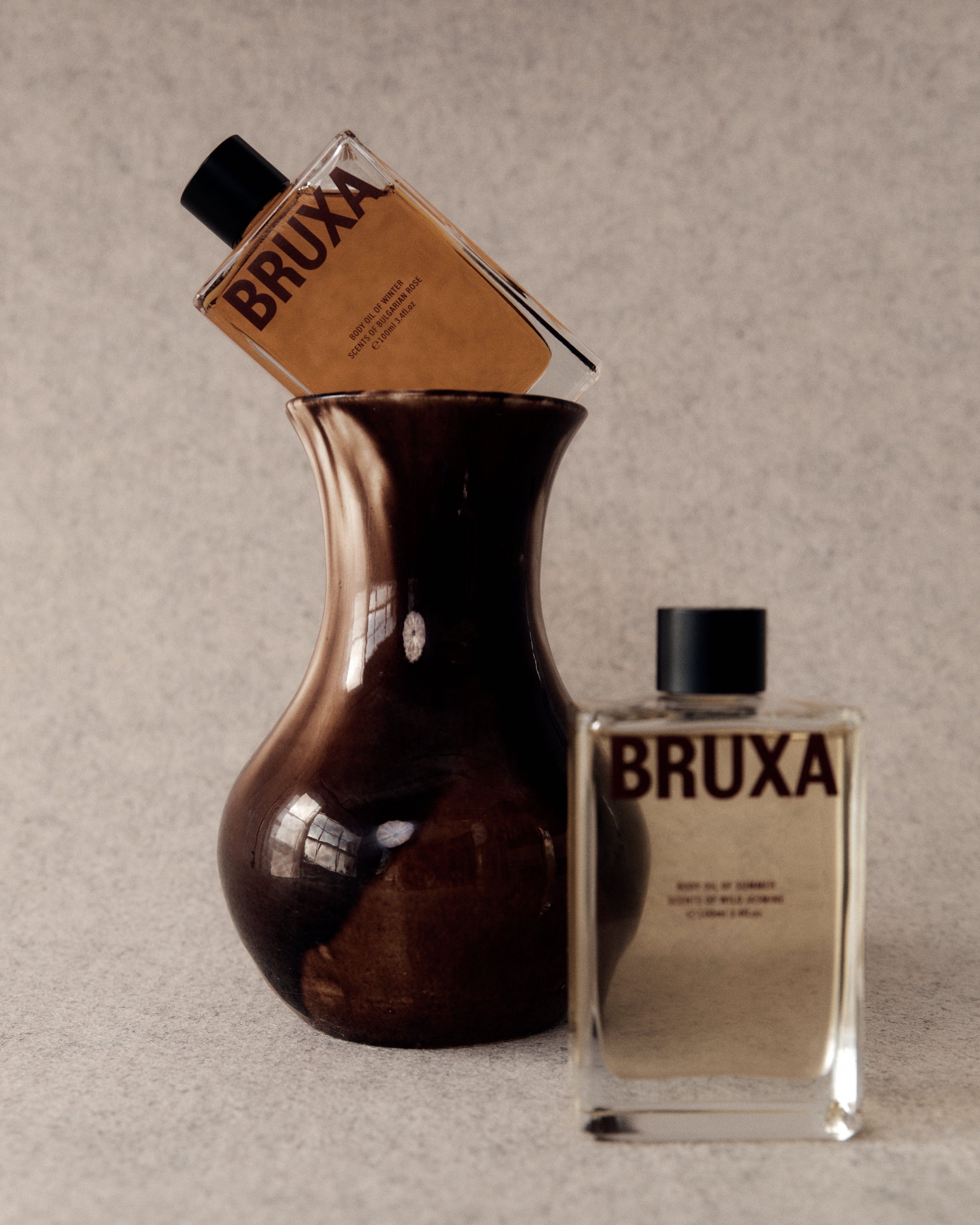 Two 'BRUXA' perfume bottles on a textured beige background