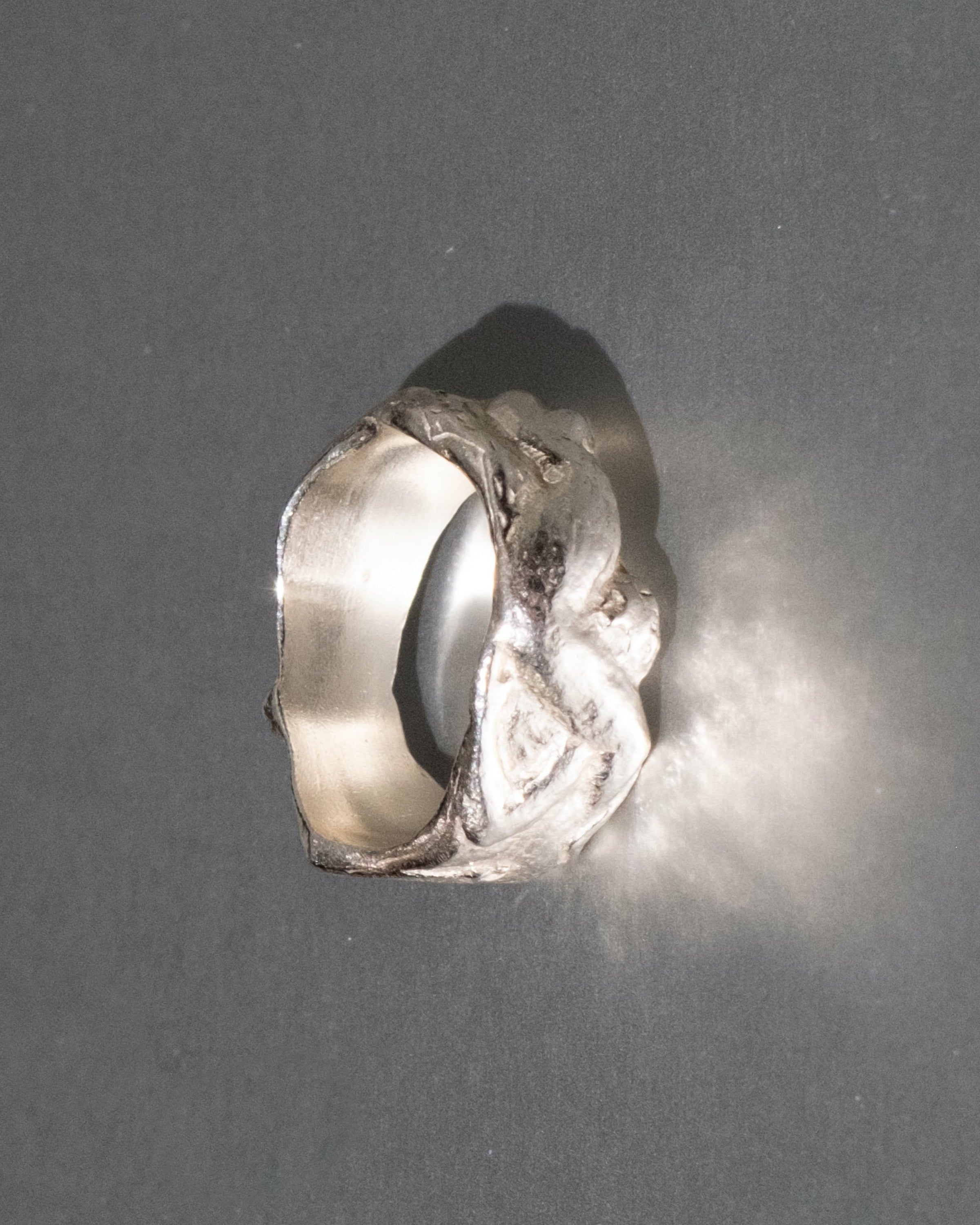 Silver ring with a textured design on a gray background