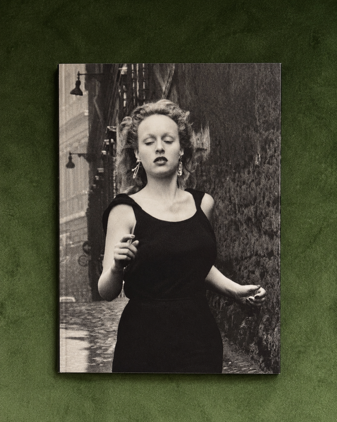 A vertical black and white photographic art print of a woman in a black dress standing outdoors, displayed against a textured dark green background.