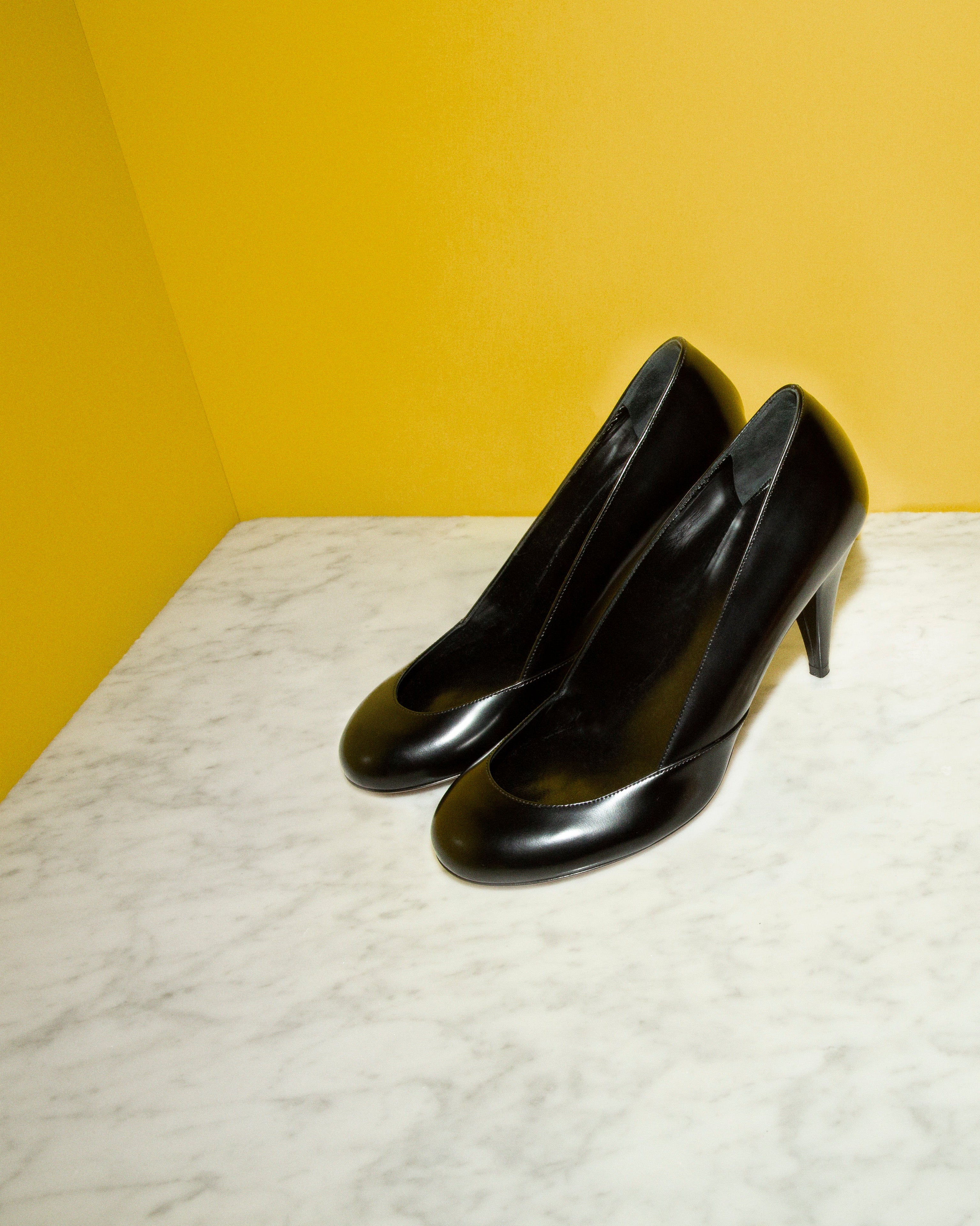 Black high-heeled shoes on a marble surface with a metallic container and ice cubes.