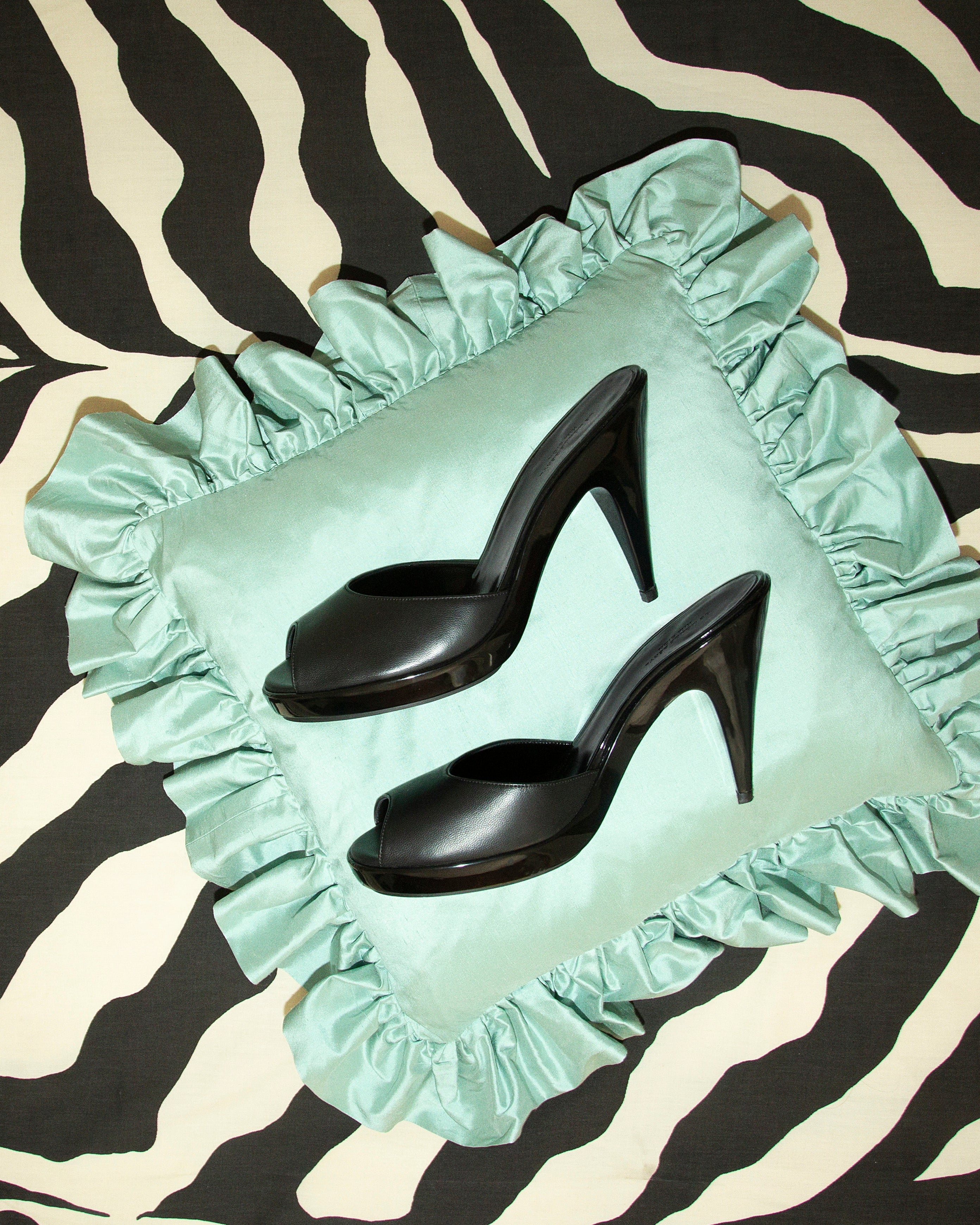 Mint green pillow with ruffles featuring black high heels on a zebra print background