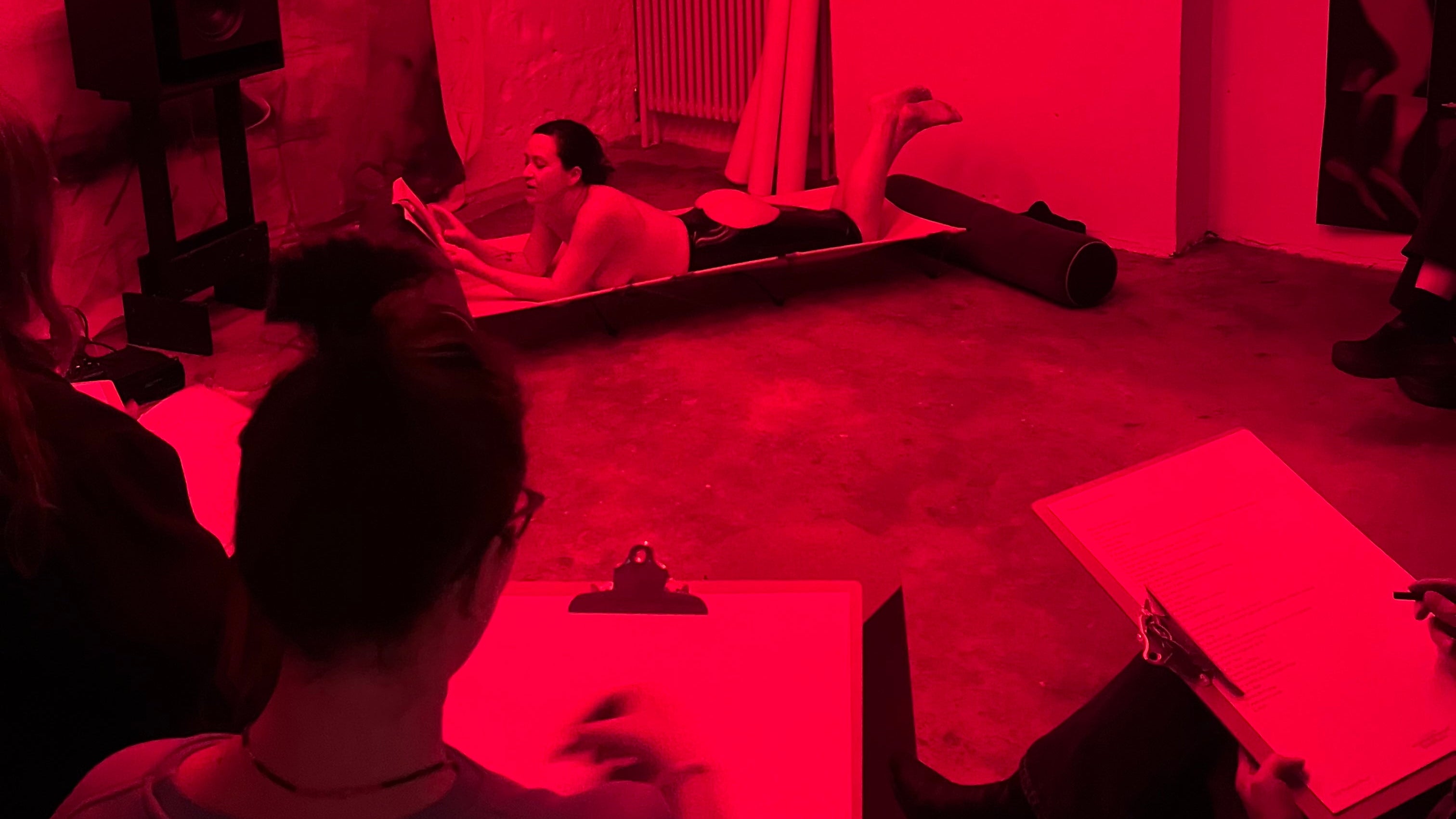 People in a room with red lighting, one person sitting on a couch reading a book.
