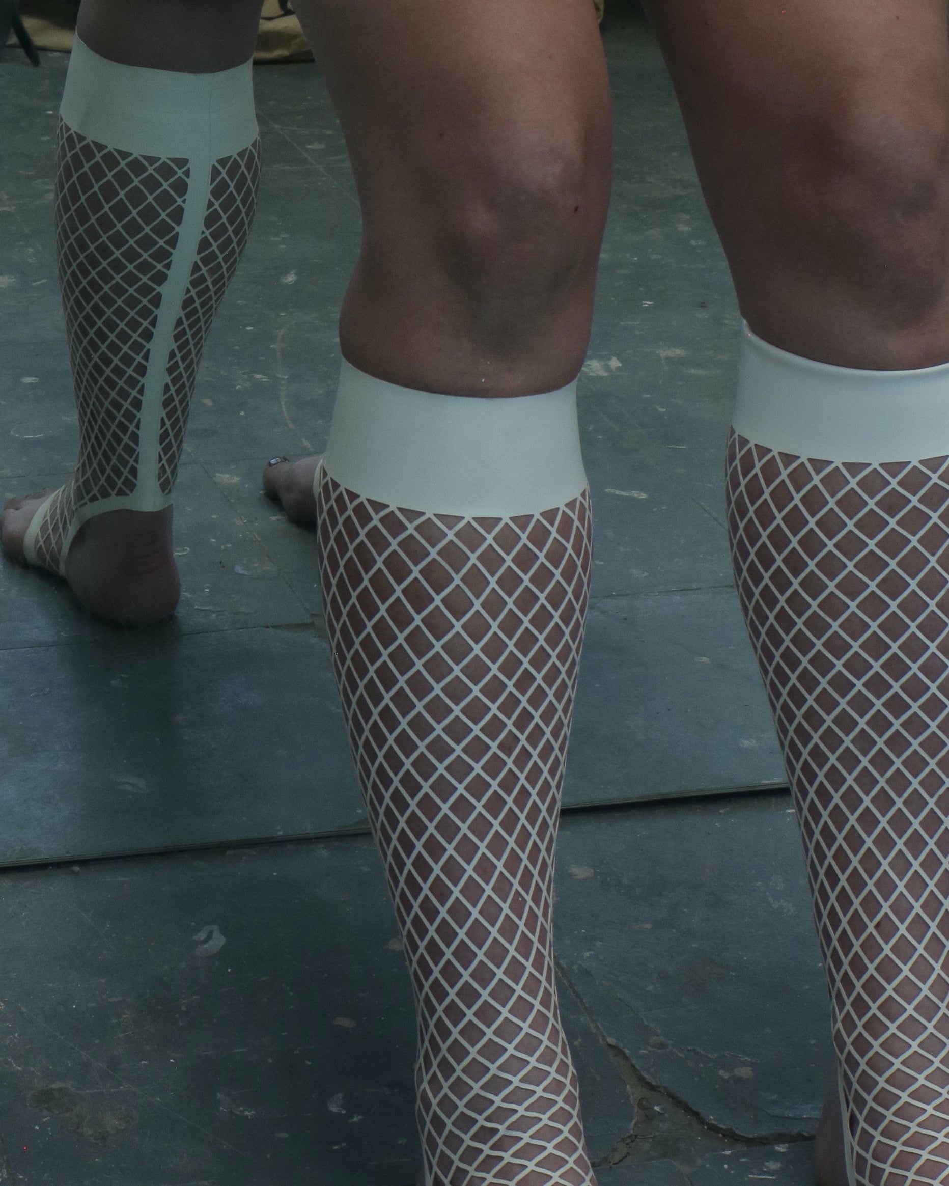 Person wearing fishnet stockings on a dark floor.