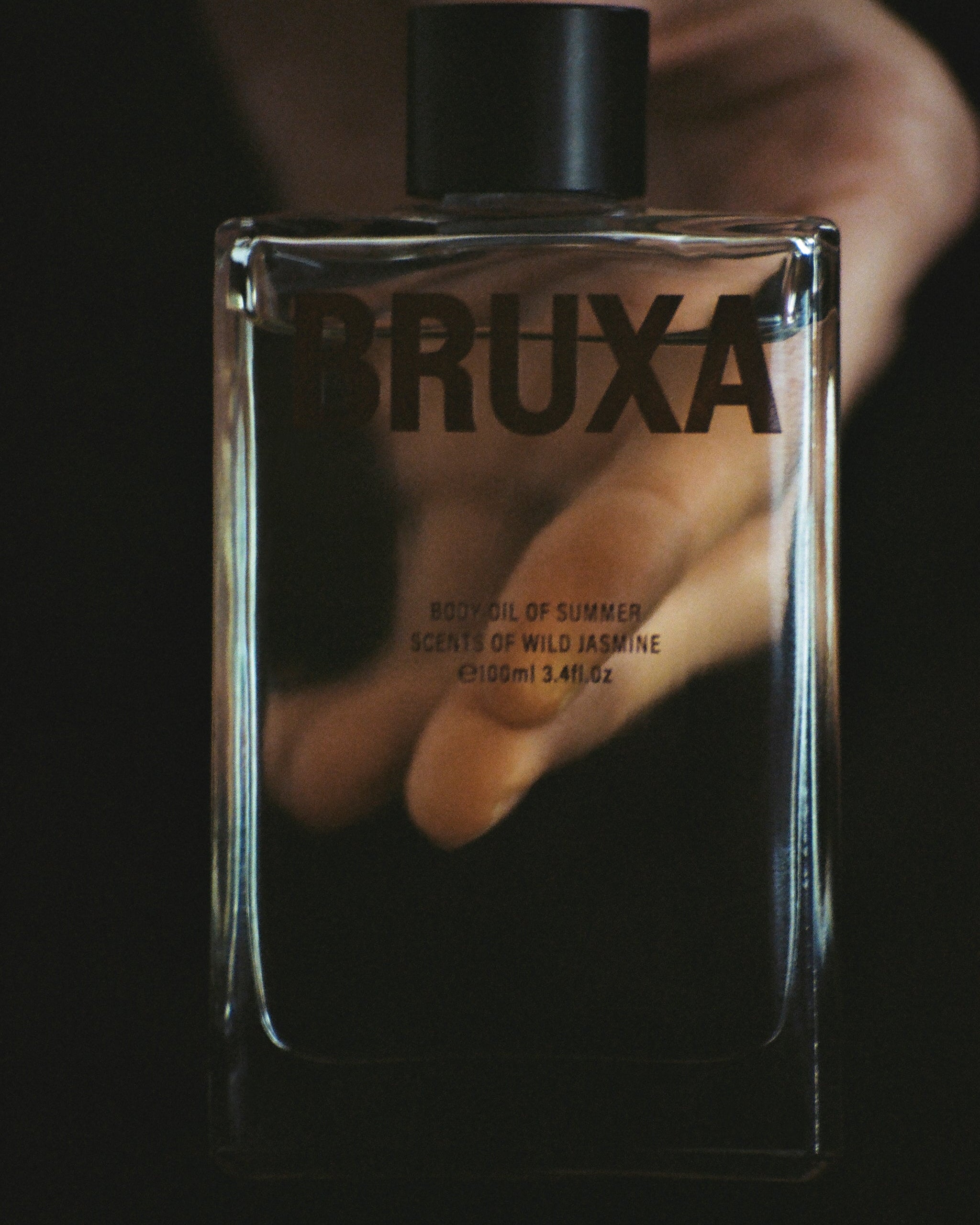 Bruxa perfume bottle held by a hand against a dark background