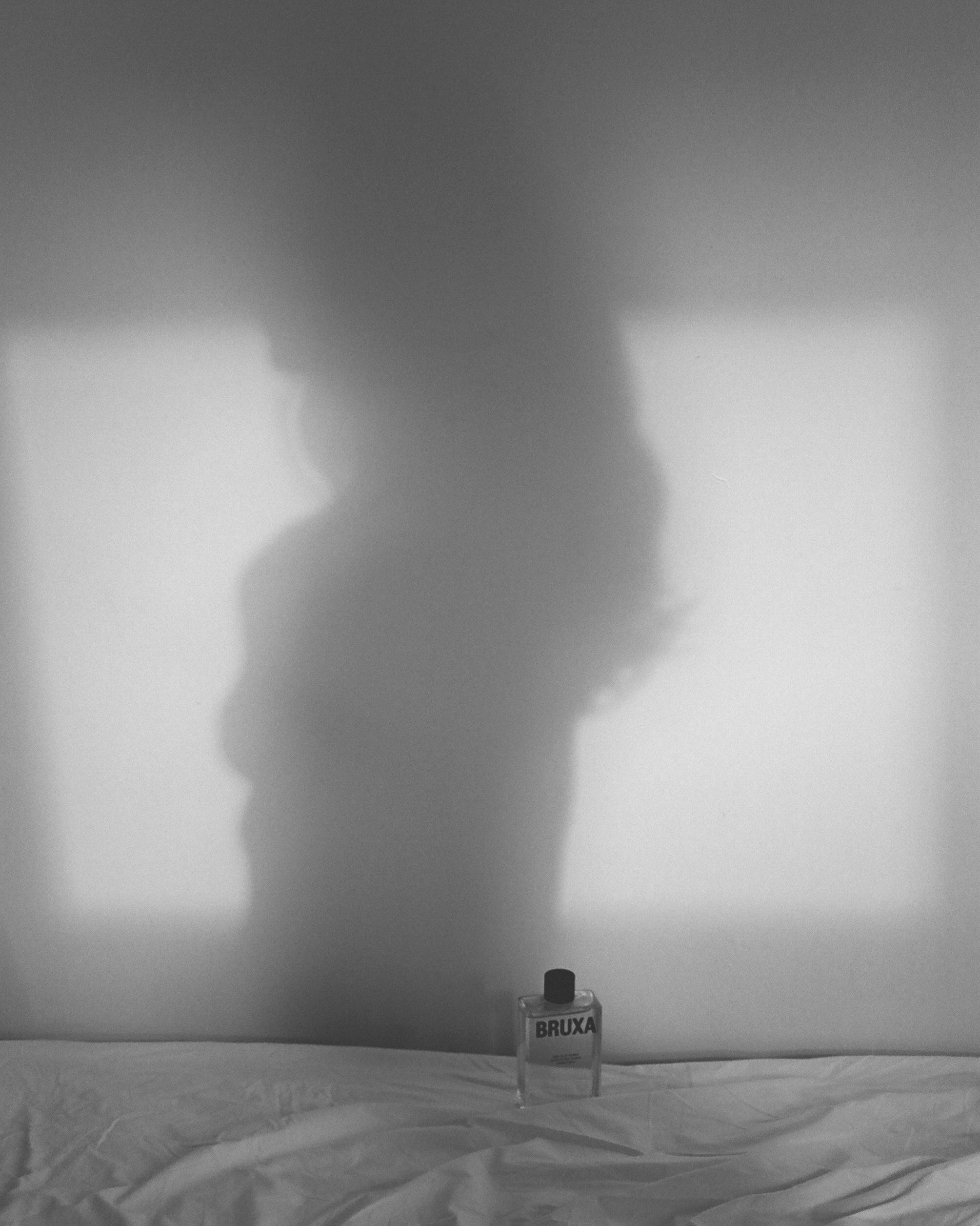 Bottle on a bed with a shadowy figure in the background